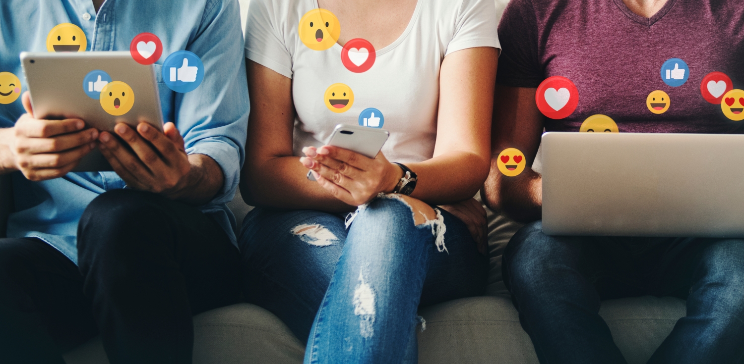Drei Leute sitzen mit verschiedenen Geräten in einer Reihe und freuen sich über Social Media